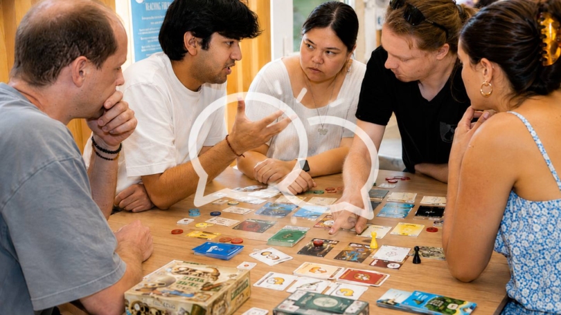 Young people discussing clues together while playing a team board game around a table
