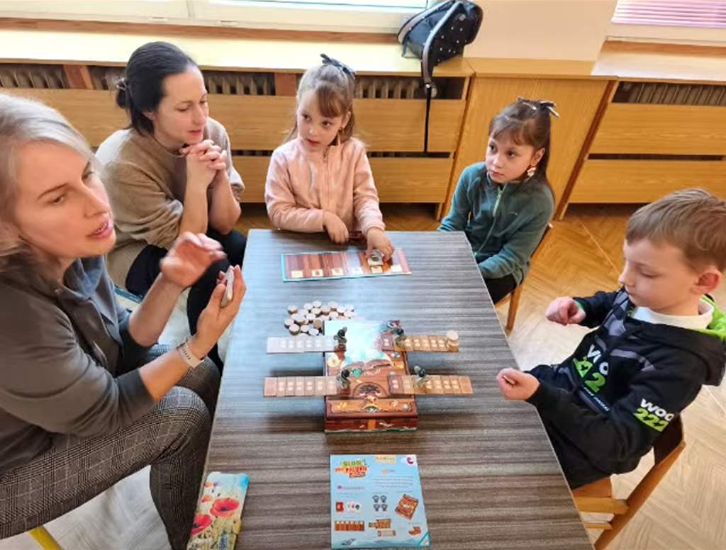 Children and an adult playing board games together during Game On Sunday at Centrum Petrklíč in Czechia.